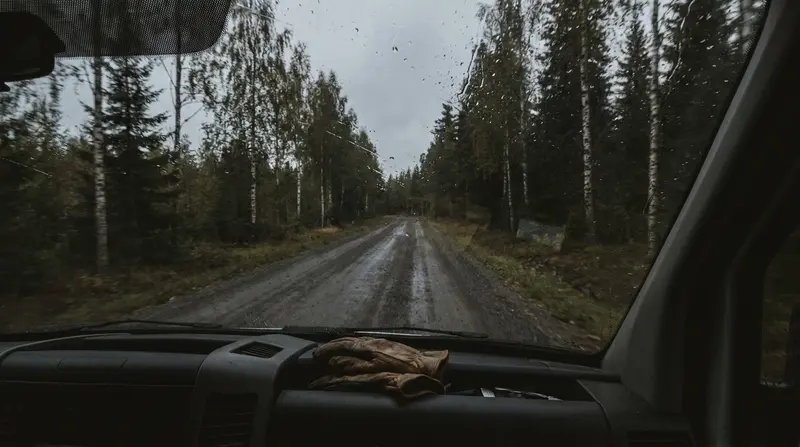 Näkymä pakettiauton tuulilasista sateiselle soratielle